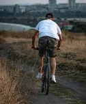 Un hombre de espaldas rueda en bicicleta por un camino de tierra, con la ciudad al fondo